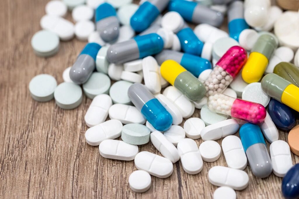 Assorted colorful capsules and white tablets scattered on wooden surface.